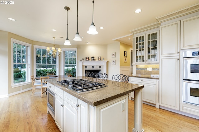 kitchen with decorative light fixtures, light wood finished floors, stainless steel appliances, recessed lighting, and glass insert cabinets