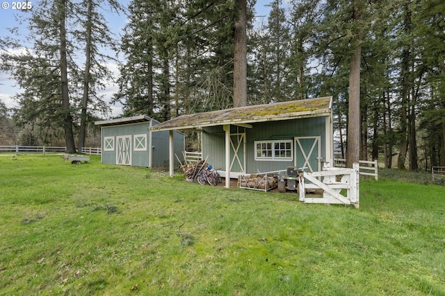 back of house featuring fence, an outdoor structure, and a lawn