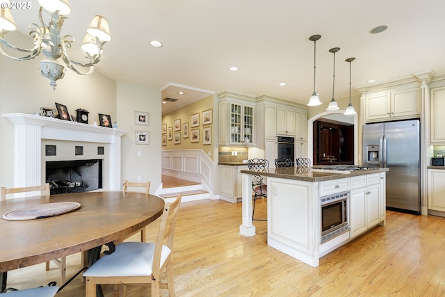 kitchen featuring stainless steel appliances, a fireplace, a kitchen island, light wood finished floors, and glass insert cabinets