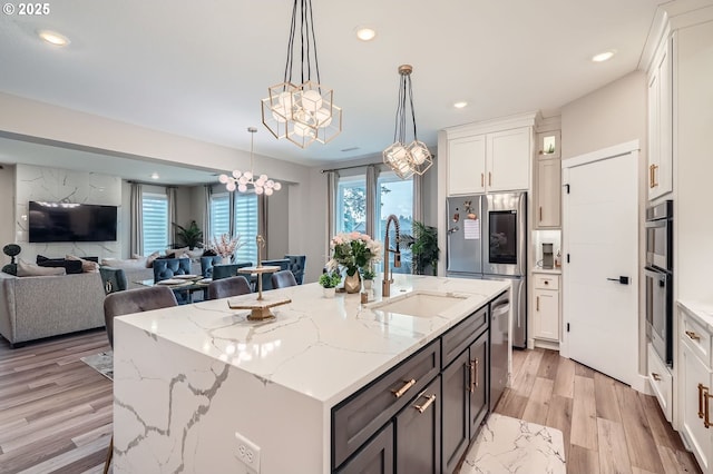 kitchen featuring a notable chandelier, a sink, open floor plan, appliances with stainless steel finishes, and white cabinets