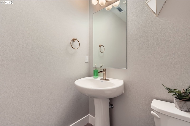 bathroom featuring visible vents, toilet, and a textured wall