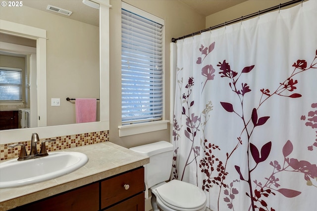 bathroom featuring a healthy amount of sunlight, toilet, vanity, and backsplash