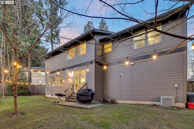 back house at dusk with a lawn, a patio, and central air condition unit