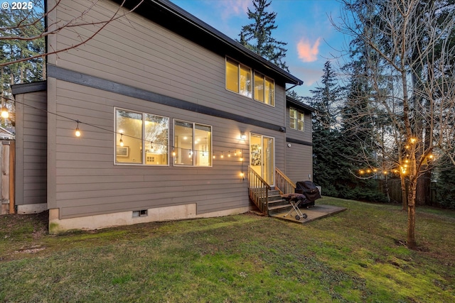 back house at dusk featuring a yard and a patio area