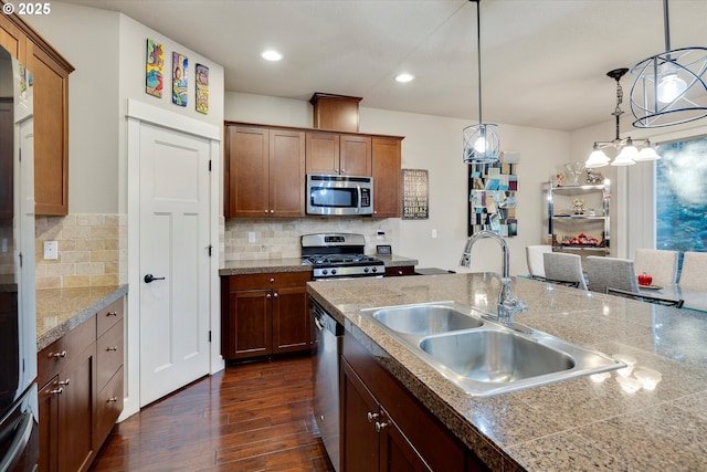 kitchen featuring dark wood-type flooring, sink, hanging light fixtures, stainless steel appliances, and backsplash