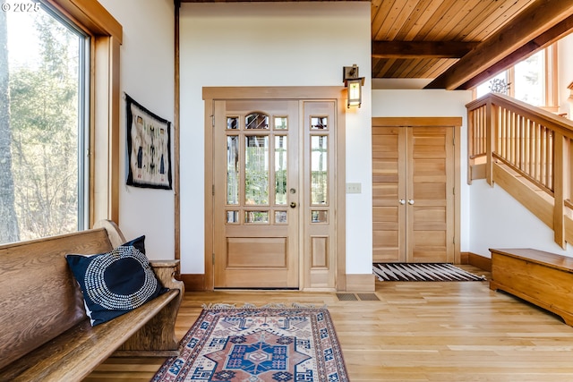 foyer with beam ceiling, light wood-type flooring, wooden ceiling, baseboards, and stairs