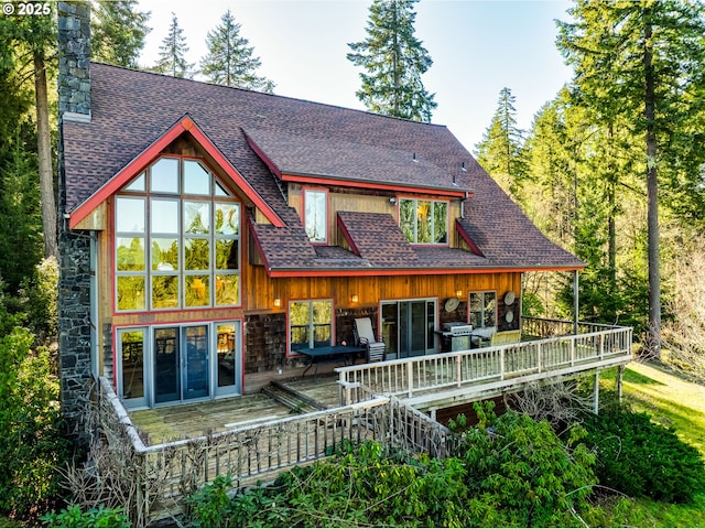 back of property with a shingled roof, a chimney, and a wooden deck