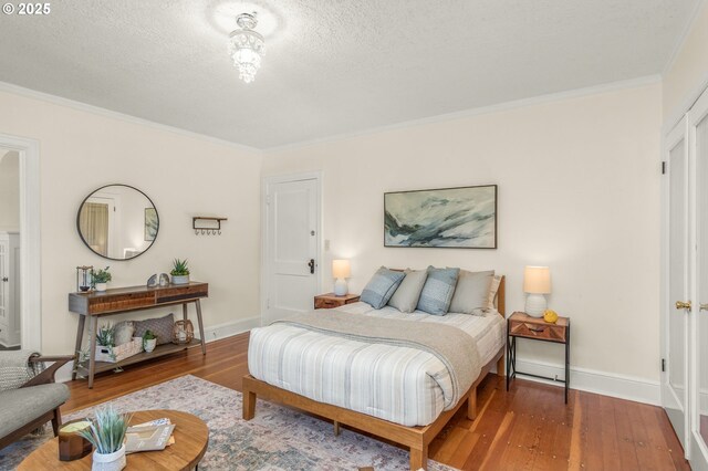 bedroom featuring crown molding, wood finished floors, a textured ceiling, and baseboards