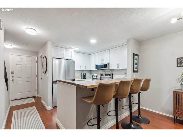 kitchen with baseboards, a peninsula, dark wood finished floors, and appliances with stainless steel finishes