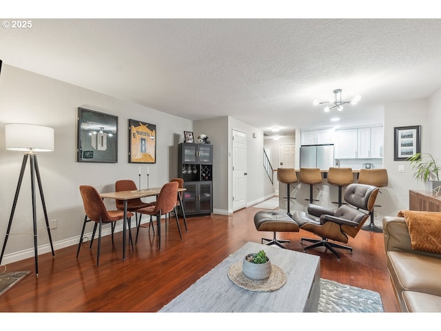 living room featuring a textured ceiling, baseboards, an inviting chandelier, and wood finished floors