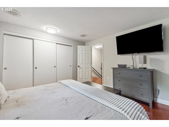 bedroom featuring baseboards, a closet, a textured ceiling, and dark wood-type flooring
