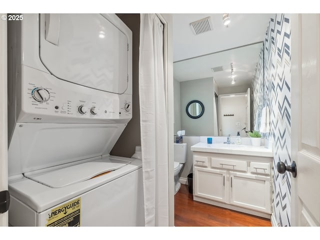 washroom with stacked washing maching and dryer, visible vents, a sink, and wood finished floors