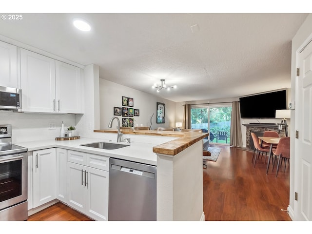 kitchen with a sink, stainless steel appliances, open floor plan, white cabinetry, and a peninsula