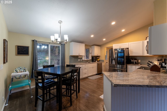 kitchen with appliances with stainless steel finishes, kitchen peninsula, white cabinets, lofted ceiling, and tasteful backsplash