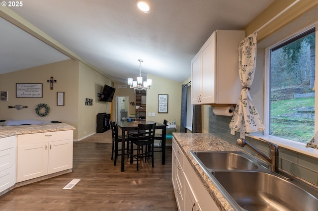 kitchen with tasteful backsplash, lofted ceiling, an inviting chandelier, white cabinets, and sink