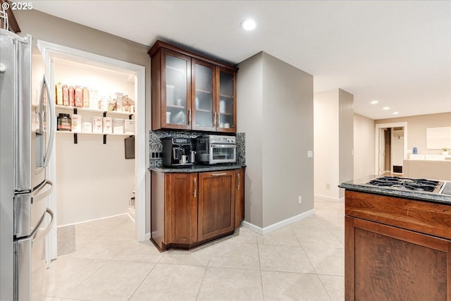 kitchen featuring light tile patterned floors, baseboards, stainless steel fridge with ice dispenser, glass insert cabinets, and backsplash