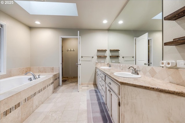 bathroom with a garden tub, a skylight, double vanity, and a sink