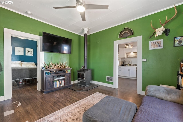 living area with ceiling fan, visible vents, crown molding, a wood stove, and dark wood-style floors