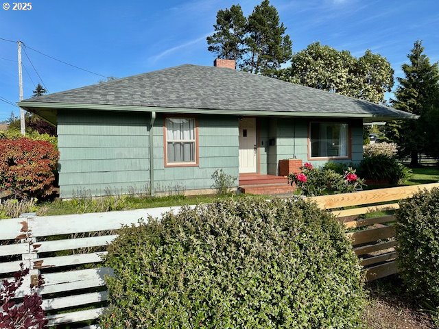 view of front of house with roof with shingles, fence, and a chimney