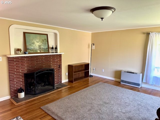 living room featuring crown molding, baseboards, a brick fireplace, and wood finished floors