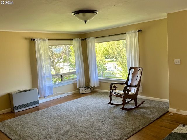 sitting room featuring heating unit, baseboards, and wood finished floors