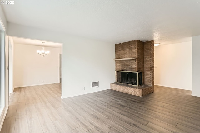 unfurnished living room with a fireplace, light wood-type flooring, a textured ceiling, and an inviting chandelier