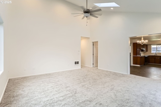 carpeted spare room featuring ceiling fan with notable chandelier, sink, high vaulted ceiling, and a skylight