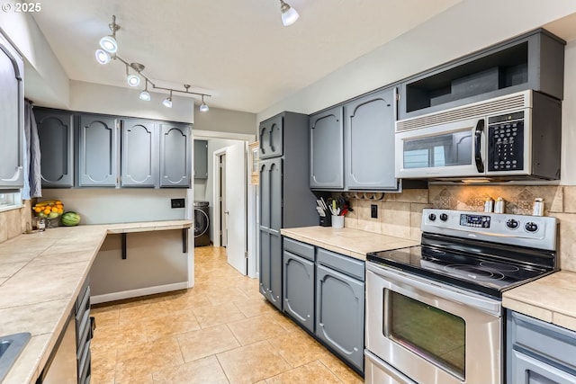 kitchen with stainless steel range with electric cooktop, decorative backsplash, light tile patterned floors, tile counters, and washer / dryer