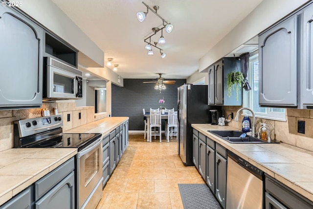 kitchen with ceiling fan, sink, tile counters, backsplash, and appliances with stainless steel finishes