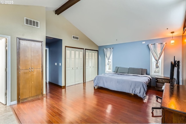 bedroom with beamed ceiling, wood-type flooring, two closets, and high vaulted ceiling