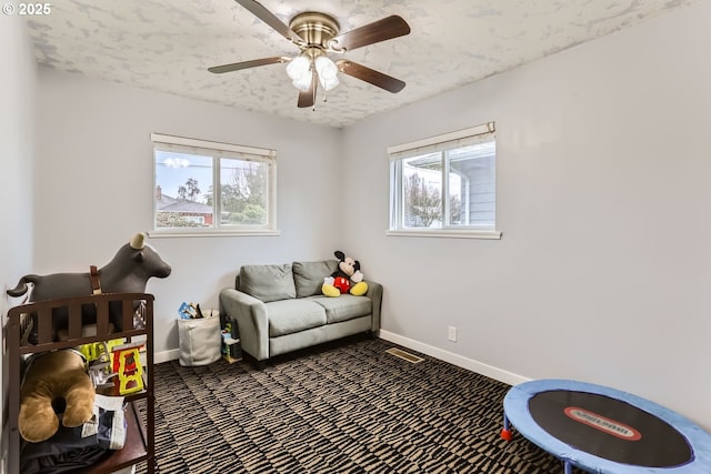 sitting room featuring a wealth of natural light, ceiling fan, dark carpet, and a textured ceiling