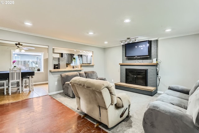 living room featuring ceiling fan, crown molding, light hardwood / wood-style floors, track lighting, and a fireplace