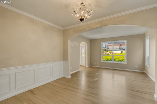 unfurnished room featuring arched walkways, ornamental molding, wainscoting, and light wood-style floors