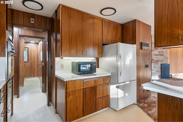 kitchen featuring white refrigerator, tasteful backsplash, stainless steel oven, and wood walls