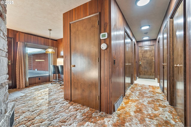 corridor featuring light colored carpet, a textured ceiling, and wood walls