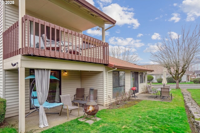 back of house with an outdoor fire pit, a balcony, a yard, a tiled roof, and a patio area