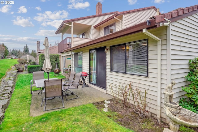 rear view of house featuring a balcony, a yard, a chimney, and a patio