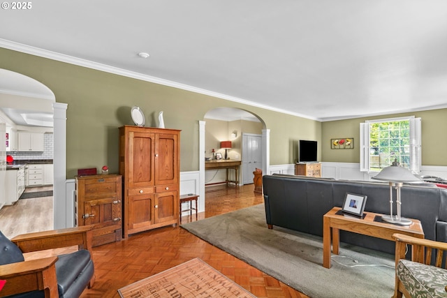 living area featuring wainscoting, crown molding, and arched walkways