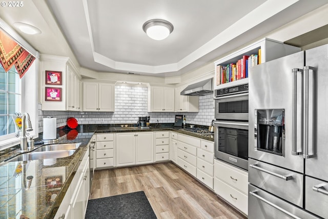 kitchen with light wood finished floors, a sink, white cabinetry, wall chimney range hood, and stainless steel appliances