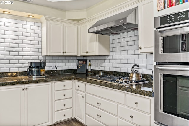 kitchen with wall chimney exhaust hood, decorative backsplash, tile counters, white cabinets, and appliances with stainless steel finishes