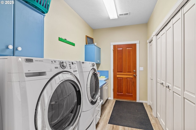 laundry area with cabinet space, a textured ceiling, visible vents, washing machine and clothes dryer, and light wood-style flooring