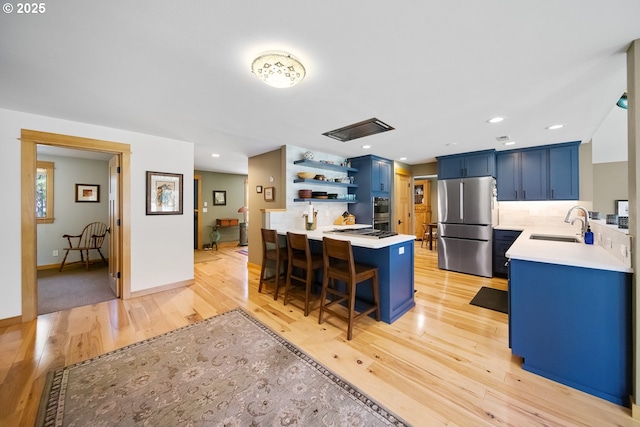 kitchen with a sink, stainless steel appliances, open shelves, a peninsula, and blue cabinets