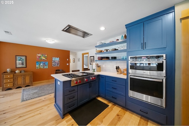 kitchen featuring appliances with stainless steel finishes, blue cabinetry, a peninsula, and light countertops