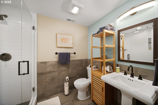 full bath featuring a shower stall, tile walls, toilet, a sink, and visible vents