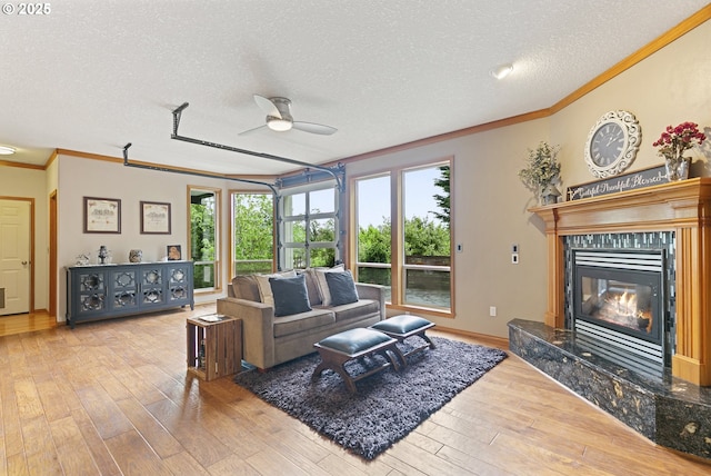 living area with crown molding, a ceiling fan, a textured ceiling, hardwood / wood-style floors, and a high end fireplace