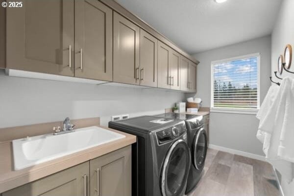 laundry room with baseboards, washing machine and dryer, light wood-style flooring, cabinet space, and a sink