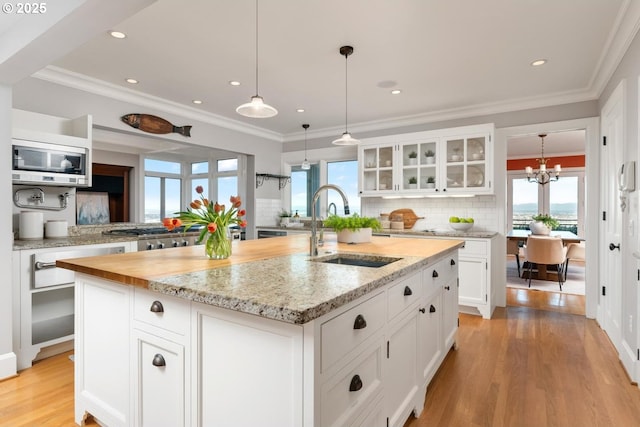 kitchen with stainless steel appliances, sink, pendant lighting, a center island with sink, and white cabinets