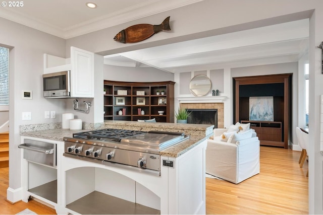 kitchen featuring white cabinets, light hardwood / wood-style flooring, a fireplace, appliances with stainless steel finishes, and light stone counters