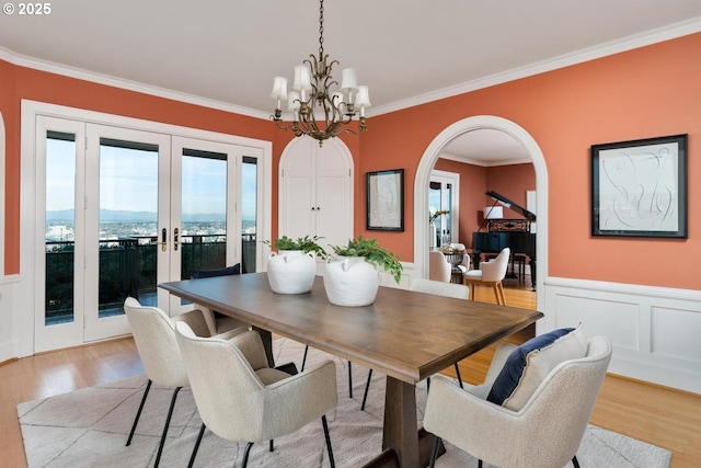 dining area with french doors, ornamental molding, a notable chandelier, and light wood-type flooring