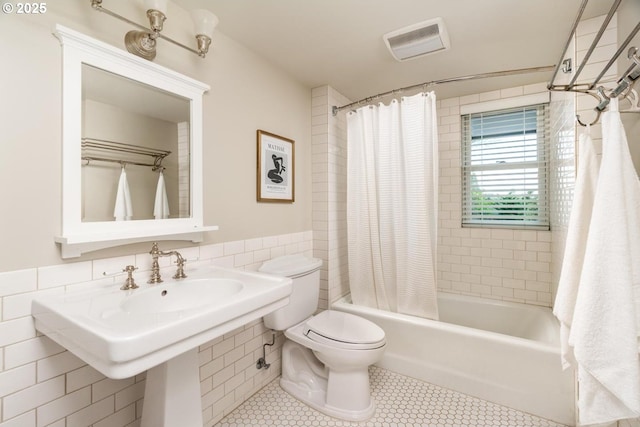 bathroom with tile patterned flooring, shower / bath combination with curtain, toilet, and tile walls